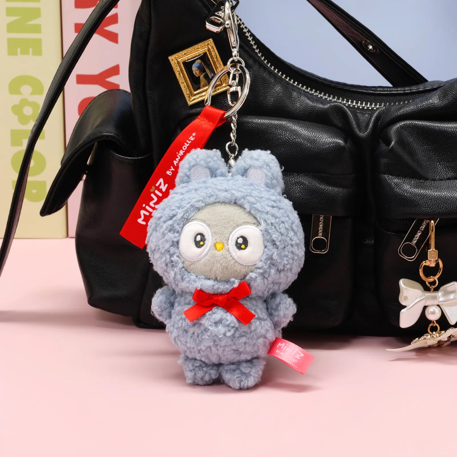 Front view Bunny Costume Owlyroll Plush Charm in front of Black Purse