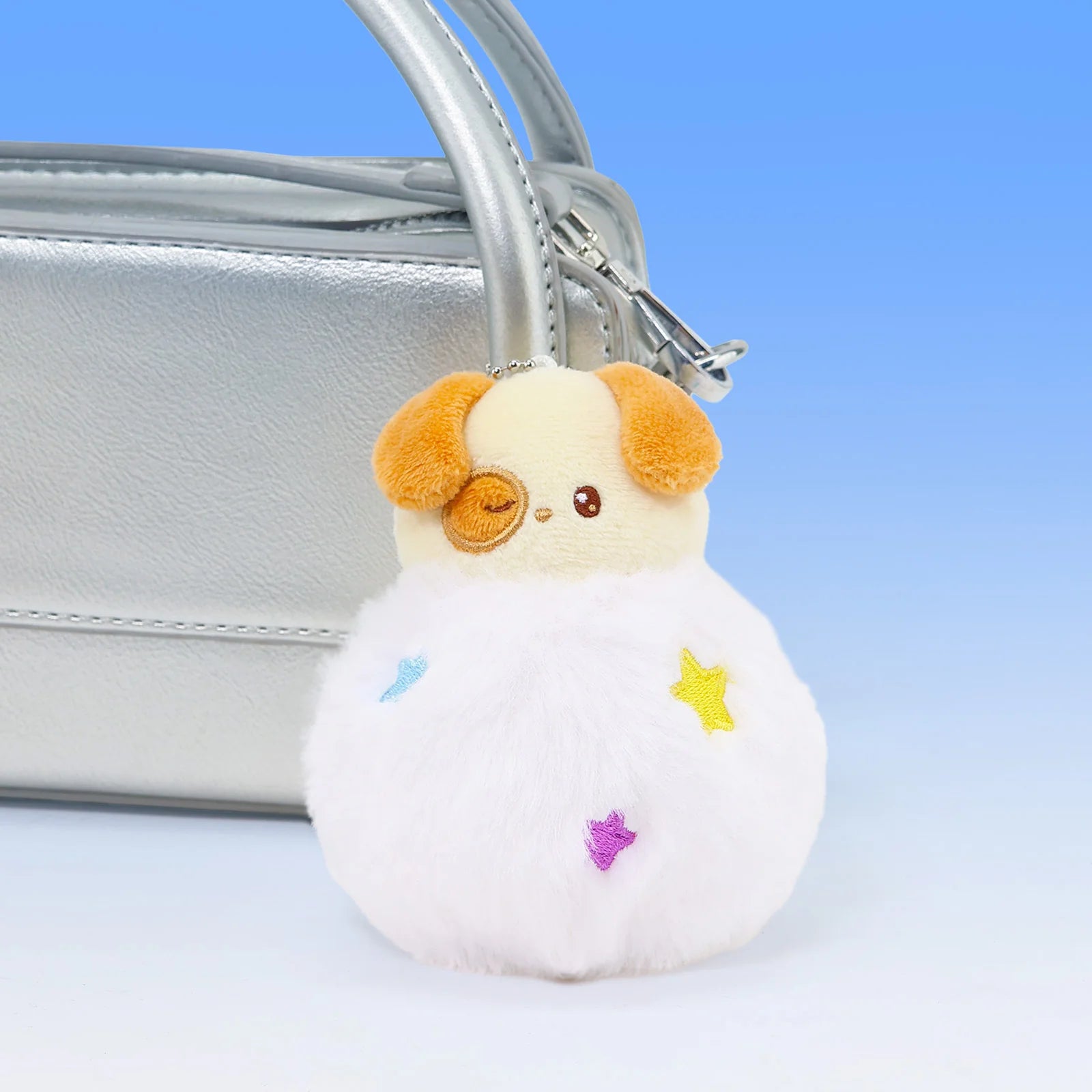Front view Fluffy Ball Puppiroll Plush Charm in front of silver purse