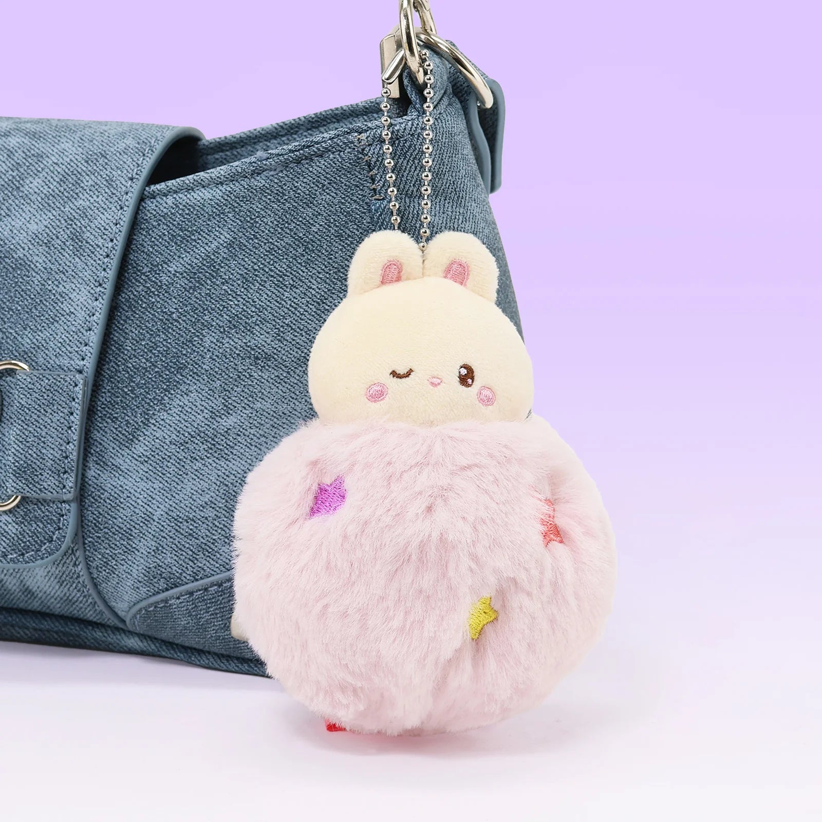 Front view Fluffy Ball Bunniroll Plush Charm in front of denim purse