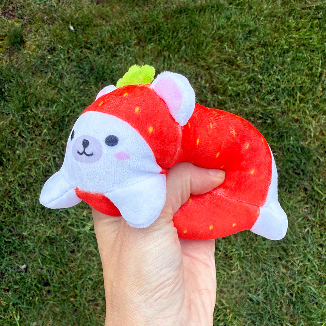 Hand squeezing a Sand-A-Roos Sensory Plush toy designed as a strawberry character, featuring a cute face and soft texture.